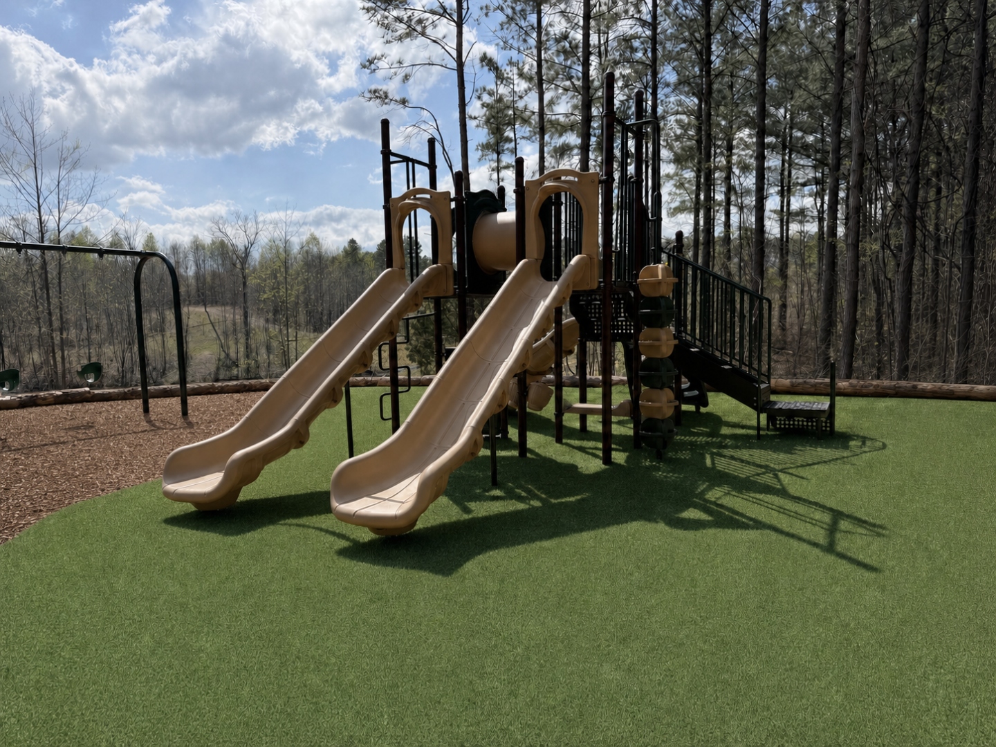 New playground with double slides, a climbing tower, and swings on safety turf at Sasquatch Farm RV Park