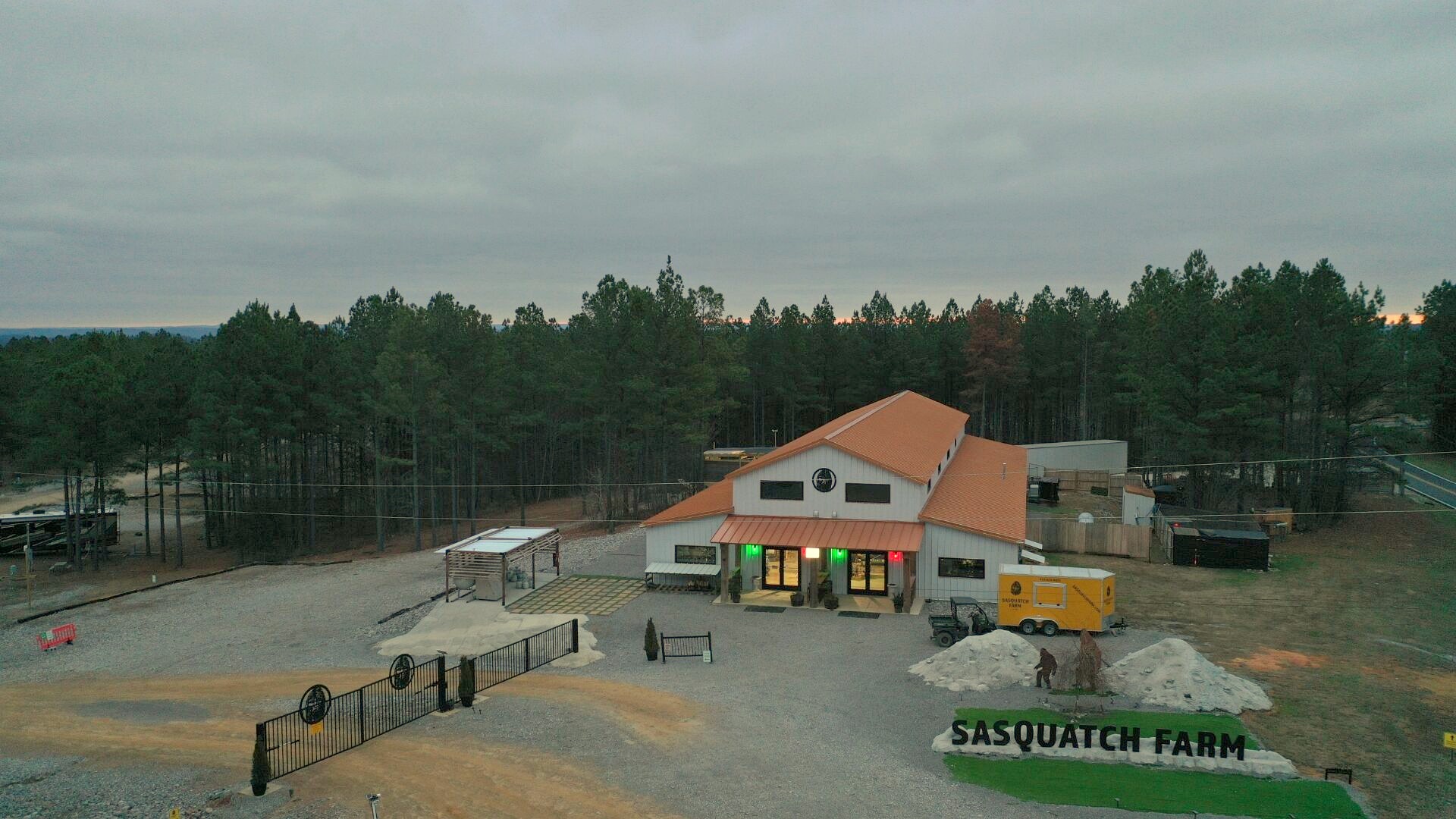 Aerial daytime view of Piggy's Store and the Sasquatch Farm RV Park check-in building, with the mountain ridge on the horizon