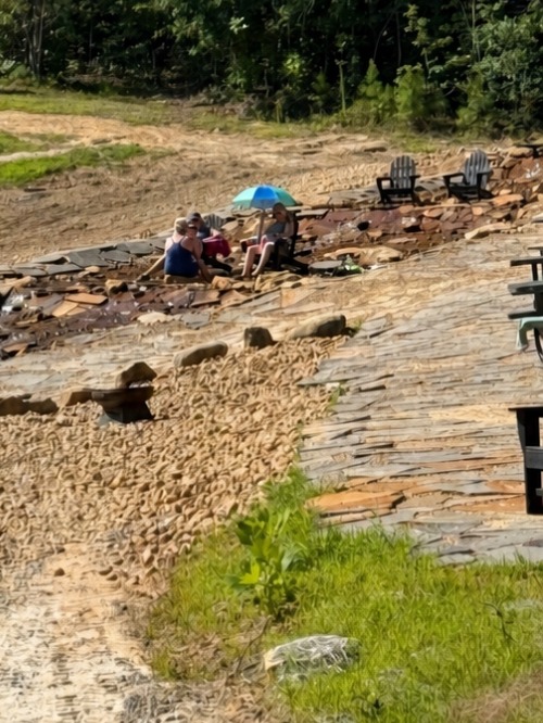 Guests relaxing in beach chairs on the sunning area at Vic and Vi's Bay, the swimming beach at Sasquatch Farm RV Park